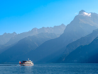 Outlines of the mountains by the swiss Lake Urnersee - Lake Luzerne - in the daytime hazy light. Tourist ship on the lake.