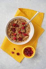 granola muesli with raspberries and almonds in a plate, with a yellow towel, small plates with raspberries and nuts nearby