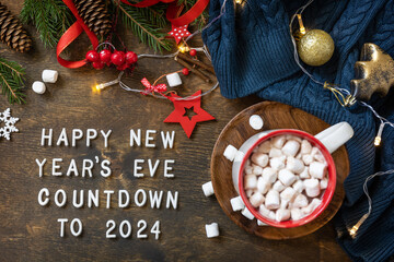 Obraz na płótnie Canvas Winter, christmas lights, cozy cup hot chocolate drink with marshmallow on wooden table background. View from above with english text Happy New Year's Eve countdown to 2024.