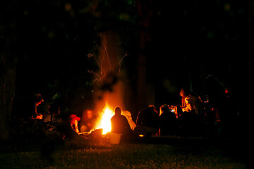 People around a bonfire at night. Figure silhouettes. Unrecognizable. Warm atmosphere.