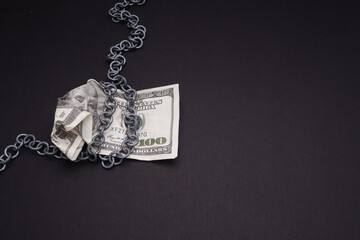 One hundred American dollar banknotes crumpled with chain wrap on a black background.