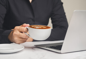 Businesswoman holding a cup of coffee while working at a desk.