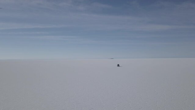 Aerial drone shot of a 4x4 offroad vehicle driving on the Salar de Uyuni salt lake around the isla pescado, fish island, on the biggest salt flat in the world in high altitude of the Andes in the Boli