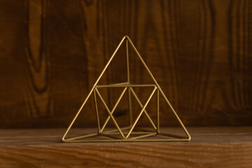 Metal pyramid of golden color in the shape of a wire on a wooden background. Interior Design