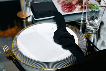 A black napkin elegantly knotted and placed upon a refined plate, adorning a mirrored table within...