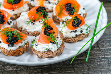 Cocktail canapes with smoked salmon, cream cheese and caviar on rye bread - gourmet party food.