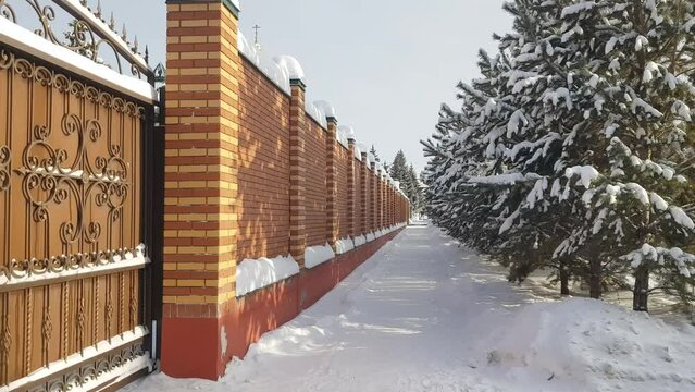 4k, video, modern brick fence along a snow-covered sidewalk, in front of a row of tall fir trees, urban landscape