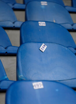 Close-up of a seat in a stadium with a little number plate half falling off