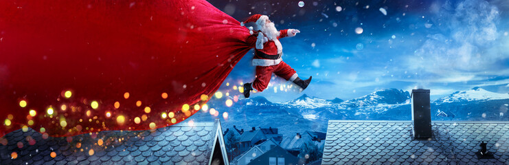 Santa Claus With Red Big Bag Jumping On Roofs In Snowy Winter Landscape - Fast Delivery Present