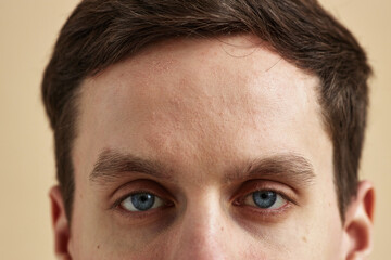 Obraz premium Close up macro shot of young man with striking blue eyes looking at camera against neutral background, copy space