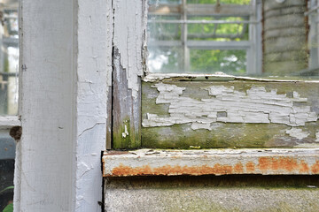 Wooden window frame damaged paint. Old window frame needing replacement. Paint job required. Old paint flaking. House maintenance needed concept.