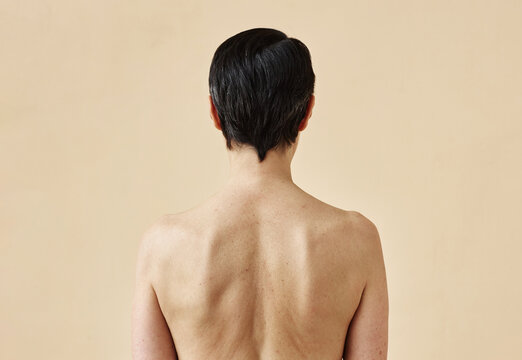 Rear view of unrecognizable adult woman with bare back standing against minimal beige background, copy space