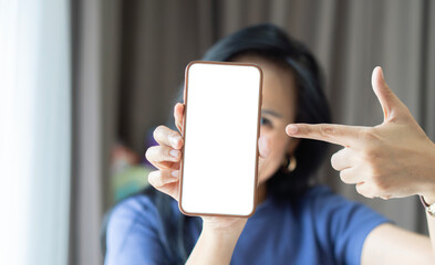 Smiling happy woman of Asian in blue sweater point finger on mobile cell phone with blank screen.