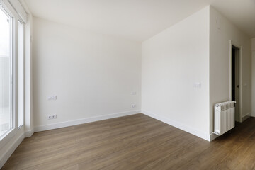 Empty room in a house with off-white painted walls, wooden floors and white aluminum radiators