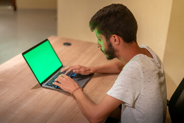 A young freelancer sitting in front of his MacBook Pro with green screen on a wooden desk