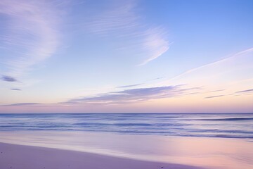 Fototapeta na wymiar うっすらとした雲と穏やかな波が打ち寄せるパステルカラーのビーチの日の出