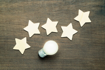 Wooden five stars symbol along with glowing light bulb on wood background, tips for top results,...