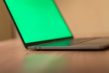 A MacBook Pro with green screen on a wooden desk - obrazy, fototapety, plakaty