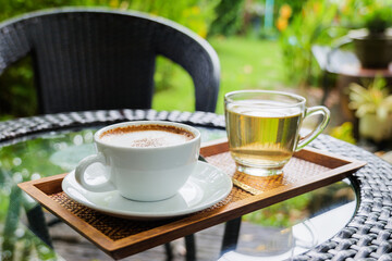 Cappuccino in white mug with tea water on the wood tray in the garden backyard