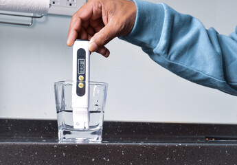 Man hand holding a digital water quality tester device in a glass of tap water on wooden...