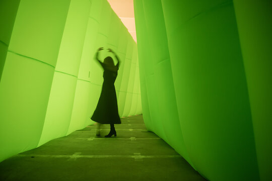 silhouette of a woman in a black dress dancing in a green tunnel 