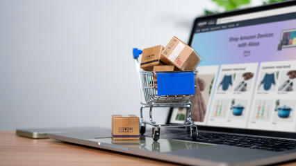 Shopping cart and product boxes placed on laptop computer represent online shopping concept,...