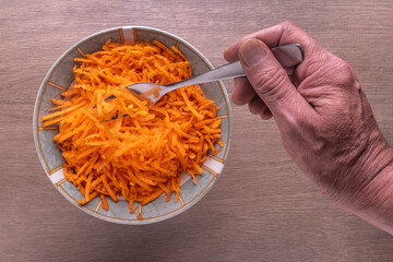 grated carrots in a bowl and a Human hand