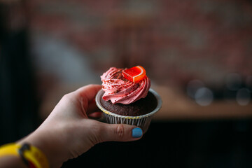 Cupcake with pink cream and red marmalade in the hand of a woman with a blue manicure on a kitchen background