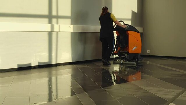 A young woman washes floors with a floor scrubber for industrial premises.