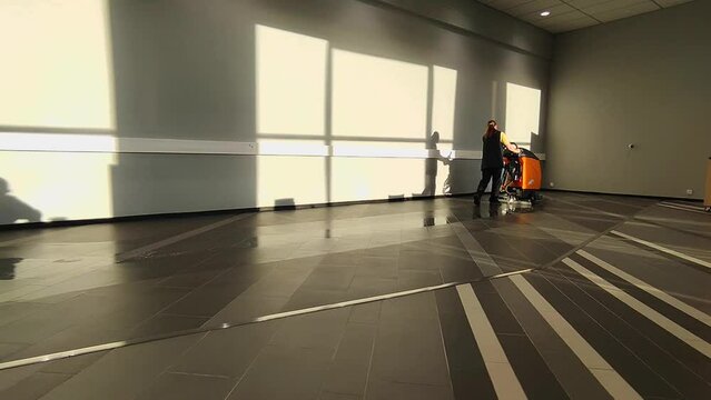 A young woman washes floors with a floor scrubber for industrial premises.
