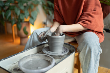 Hands of craftswoman ceramist working sitting in cozy workshop using potter wheel for make clay tableware. Process of creating handmade chinaware in art studio for creative entrepreneurs and artisans 