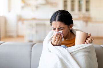 Cold And Flu Symptoms . Sick indian woman covered in blanket blowing nose