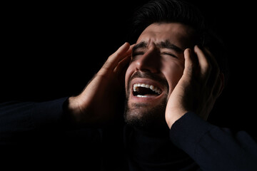 Stressed Young hopeless man screaming and shouting Frustrated handsome man agonizing and torturing expression He get maddening and overwhelming rage in the dark room black background Agressive man - obrazy, fototapety, plakaty