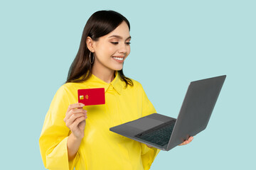 Obraz premium Beautiful young woman holding credit card and laptop