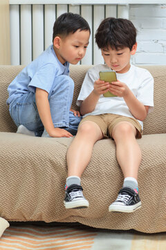 Two brothers sitting on the sofa playing mobile phones