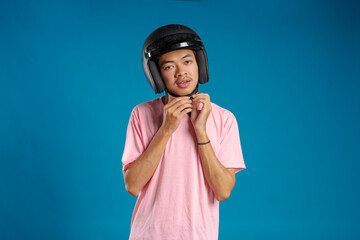 Young Asian man fastening his helmet wearing a pink t-shirt on a blue background