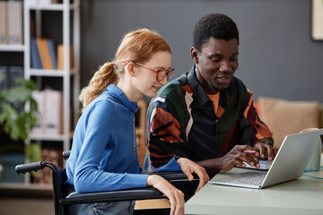 Side view portrait of smiling young woman with disability using laptop with colleague while collaborating in office