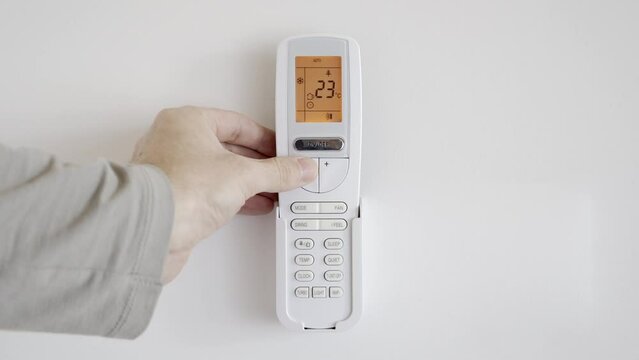 The man increases the power of the air conditioner by lowering the temperature using the remote control. The LCD display with orange backlight shows the room temperature and the automatic cooling mode