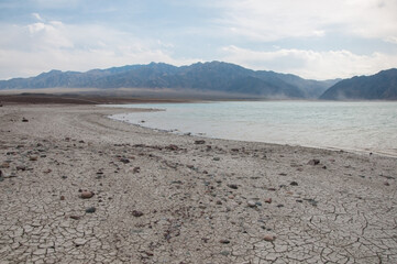 Landscape view of Bartogay lake or Bartogay reservoir with cracked soil on its coastline in the foreground, Almaty region of Kazakhstan