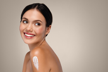 Positive young european lady with perfect skin applies cream, scrub to shoulder enjoy hygiene, look at free space