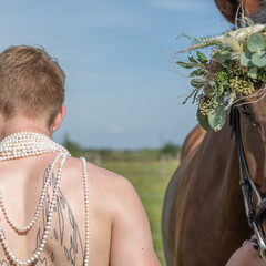 jeune homme de dos torse nu tenant un cheval avec des colliers de perles de culture