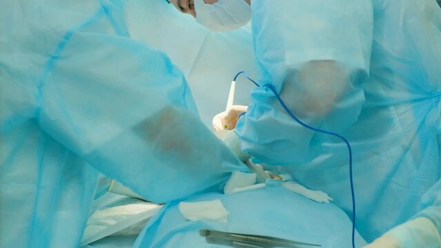 Two surgical doctors wearing masks are using specialized equipment for soft tissue cauterization during an operation.