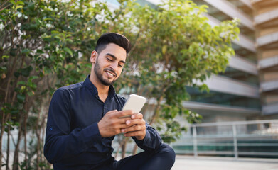 Middle Eastern business guy scrolling business app on smartphone outdoors