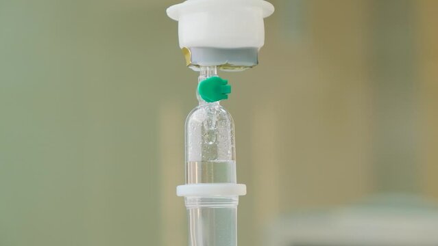 Detail close-up of vitamin IV drip chamber dripping on medical clinic. Dripping for intravenous infusion during surgery, slow motion.