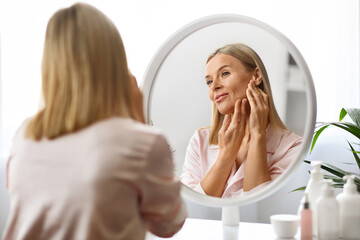 Facelift Massage. Beautiful Middle Aged Woman Massaging Face While Standing Near Mirror