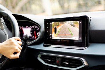 An unrecognizable person is parking a car using the auxiliary parking system using the built-in monitor in the dashboard. Rear view monitor for the car's reversing system. Safety technology equipment.