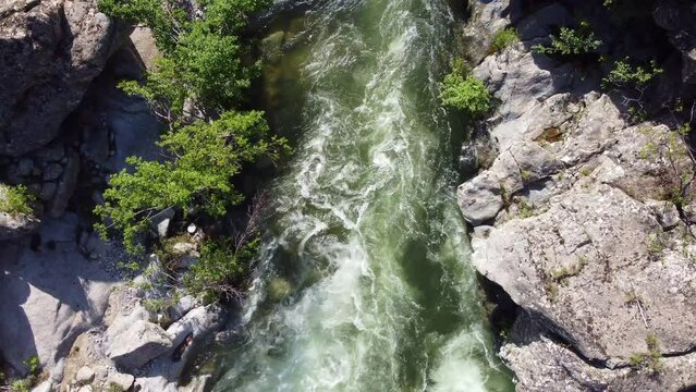 The video depicts a scenic aerial view of a rapid flowing river surrounded by rocky formations and vegetation. 