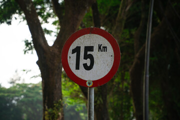 Fifteen kilometers per hour speed limit sign with trees on the background. Maximum speed on the road. Safety on road background. White round sign red border line.