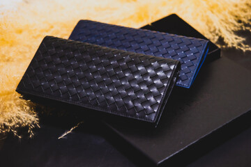 High quality genuine leather wallet in two colors, stacked on top of a black package box. On a black background over golden dried grass flowers. Studio Shot
