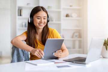 People And Technology. Asian woman in headphones using digital tablet at home